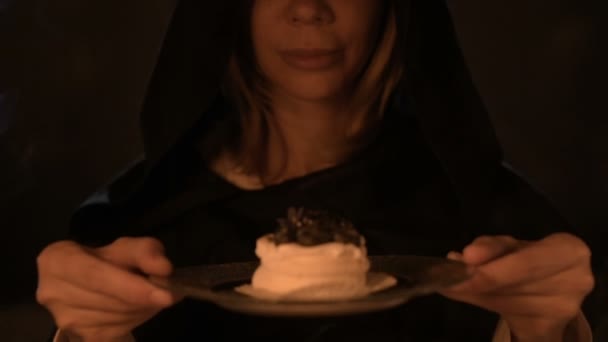 Nahaufnahme einer zufriedenen Zauberin in einem dunklen Raum bei Kerzenschein zauberte sich selbst eine Torte. hält einen Teller Kuchen niedrig Schlüssel Live-Kamera. Mystisch. kleine dof — Stockvideo