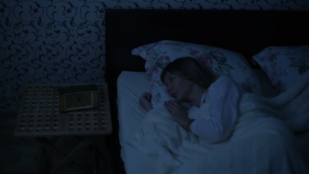 Μέσο πυροβόλησε το κορίτσι με τις πυτζάμες ξαπλωμένη στο κρεβάτι και δεν μπορεί να κοιμηθεί. γυρίζει και κοιτάζει το ταβάνι. Η επίδραση της αμερικανικής νύχτας. Απομίμηση νύχτα χαμηλό βασικό ψυχρού φωτισμού — Αρχείο Βίντεο