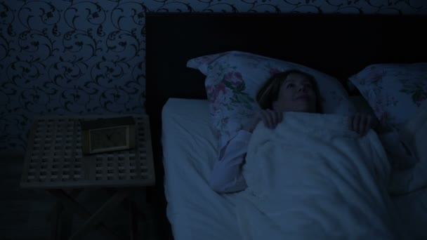 Chica de tiro mediano en pijama acostado en la cama y no puede dormir. da la vuelta y mira al techo. El efecto de la noche americana. Noche de imitación de luz fría de llave baja — Vídeos de Stock