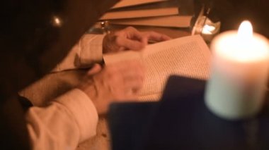 Bir büyük yakın çekim kız sihirbaz bir büyü bir kitap arıyorum mum ışığı ile karanlık bir odada. Düşük anahtar canlı kamera. Mistik. Küçük Dof