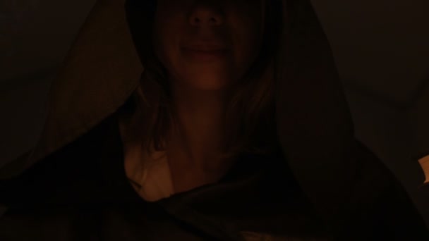 Close-up bottom of the face of the girl magician in a dark room with candlelight smiling from the flash below. Low key live camera. Mystic. Small DOF — Stock Video