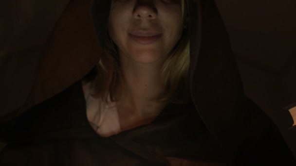 Close-up bottom of the face of the girl magician in a dark room with candlelight smiling from the flash below. Low key live camera. Mystic. Small DOF — Stock Video