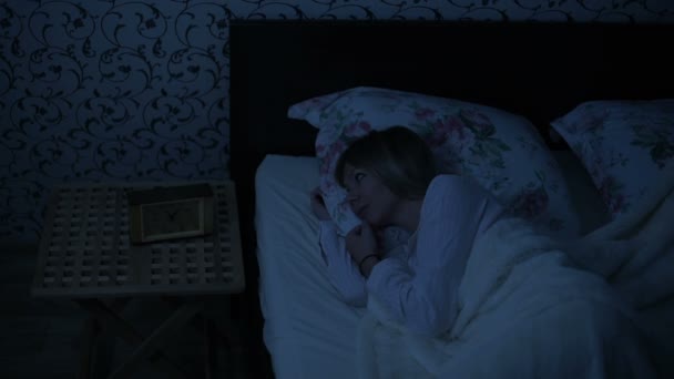 Средний выстрел девушка в пижаме лежит в постели и не может спать. поворачивается и смотрит на потолок. Эффект американской ночи. Низкий ключ холодной имитации света ночь — стоковое видео