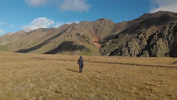 Luchtfoto van de fotograaf van een meisje lopen op een plateau in de bergen met zijn camera op de achtergrond van rotsen en bergen. Hobby's in de natuur 4k — Stockvideo