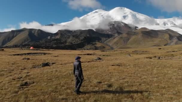 Havadan görünümü ile onun fotoğraf makinesi dağ Elbrus ve kaya arka plan üzerinde dağlarda bir plato üzerinde yürüyen bir kız fotoğrafçı. Şu anki iş doğa 4k — Stok video