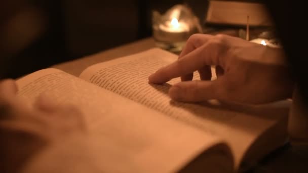 Gadis pesulap besar close-up di ruangan gelap dengan cahaya lilin mencari mantra dalam buku. Tombol rendah, kamera langsung. Mistis. DOF Kecil — Stok Video