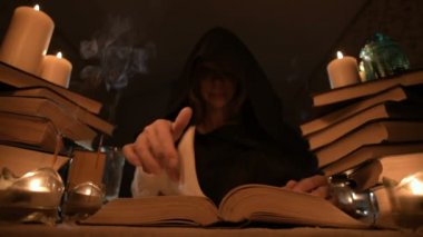 Mum ışığı ve seyir için bir kitap üzerinde bir büyü tarafından karanlık bir odada bir başlıklı orta yakın çekim kız sihirbaz. Düşük anahtar. Mistik küçük Dof