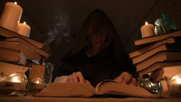 Medelstora närbild flicka trollkarl med huva i ett mörkt rum med levande ljus och letar efter en spell som välter en bok. Lågmäld. Mystic små Dof — Stockvideo