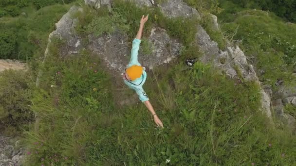 Vista aérea de una niña, los brazos extendidos, está de pie en el borde de una roca en la naturaleza. Vista desde arriba — Vídeo de stock