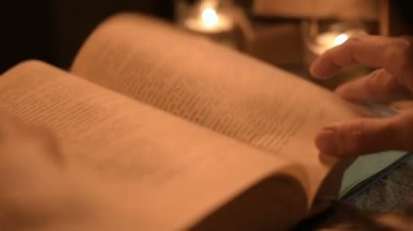 Bir büyük yakın çekim kız sihirbaz bir büyü bir kitap arıyorum mum ışığı ile karanlık bir odada. Düşük anahtar canlı kamera. Mistik. Küçük Dof
