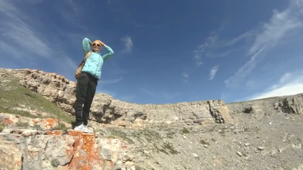 Ein Mädchen mit Rucksack geht in der Natur auf einem Plateau in der Nähe eines hohen Abgrunds spazieren. Reisekonzept — Stockvideo