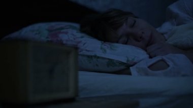 Bir kız yatakta yatarken pijama yakın çekim ve bir alarm saat bakarak uyumak yapamaz. Yüz kızlar için değişken odak saatten. Amerikan gece etkisi. Düşük anahtar soğuk ışık İmitasyon gece