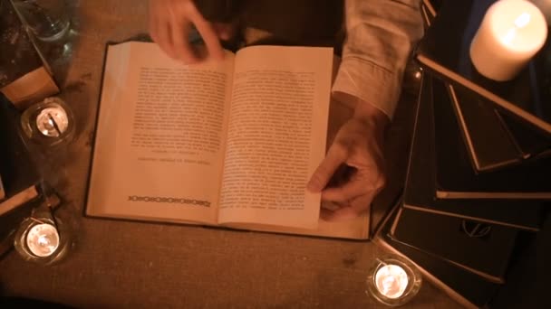 Gran mago de cerca chica en una habitación oscura con velas en busca de un hechizo en un libro. Cámara en vivo de bajo perfil. Místico. Pequeño DOF. vista desde arriba — Vídeos de Stock