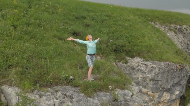 Vista aérea de uma menina alastrada para o lado fica na borda de uma rocha na natureza — Vídeo de Stock