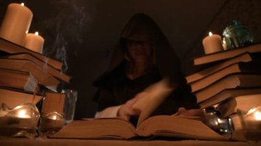 Mum ışığı ve seyir için bir kitap üzerinde bir büyü tarafından karanlık bir odada bir başlıklı orta yakın çekim kız sihirbaz. Düşük anahtar. Mistik küçük Dof