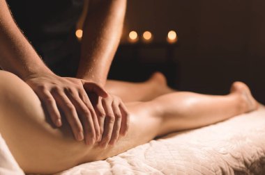 Karanlık bir odada bir masör hip bir masaj yağı ile bir kadın için yapar. Spa prosedürler kadınlar Masaj