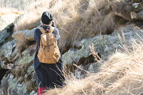 Baksidan på en attraktiv kvinnlig turist, stående i en hatt med en ryggsäck på hennes axlar som njuter av en solig eftermiddag i bergen. Begreppet livsstil resor — Stockfoto