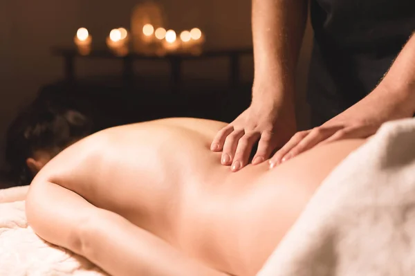 Männerhände in Nahaufnahme, die einem jungen Mädchen in einem dunklen Kosmetikbüro eine heilende Massage mit Öl verabreichen. dunkler Schlüssel — Stockfoto