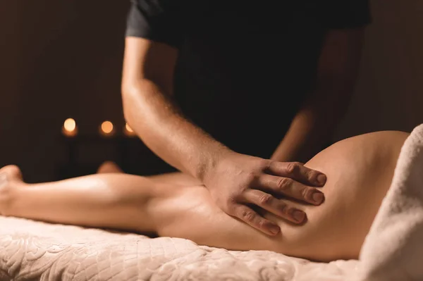 Masażysta w ciemnym pokoju robi hip masaż olejem dla kobiety. Zabiegi spa masaż kobiet — Zdjęcie stockowe