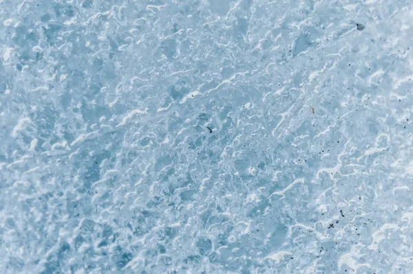 Um close-up da superfície de um fragmento de uma geleira com uma estrutura de tiras e bolhas intercaladas com areia e rocha rochosa. Textura azul gelo para a luz. DOF pequeno — Fotografia de Stock