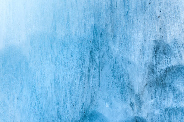 Close-up wall of a centuries-old glacier with a structure of stripes and bubbles. Ice blue light texture