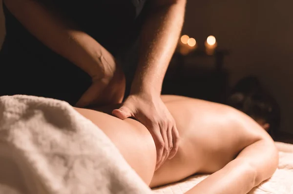 Close-up male hands doing healing massage with oil to a young girl in a dark cosmetology office. Dark key — Stock Photo, Image