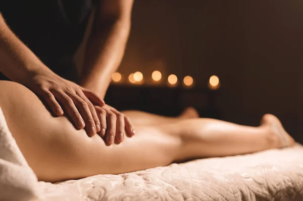 En massör i ett mörkt rum gör en hip massage med olja för en kvinna. Spabehandlingar massage kvinnor — Stockfoto