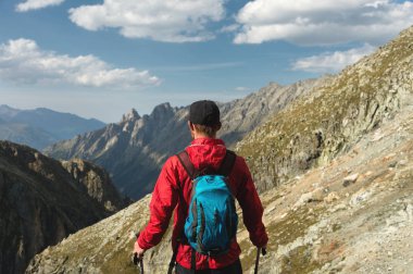 Sakallı bir adam güneş gözlüğü ve bir sırt çantası ile bir kap içinde bir kaya üzerine anlamına gelir ve bir kayalık vadide yüksek dağların içine görünüyor. Turizm ve kolay açık dağlarda trekking kavramı
