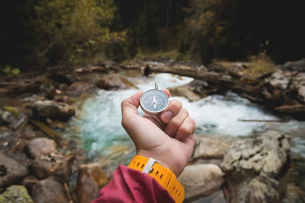 Sarı izle askısı ile güzel bir erkek el manyetik pusula bir dağ nehir kayalık taşlarla karşı bir iğne yapraklı sonbahar ormanda tutar. Kendinizi yol ve gerçeği bulma kavramı — Stok fotoğraf