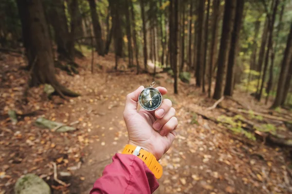 Una hermosa mano masculina con una correa de reloj amarillo sostiene una brújula magnética en el bosque otoñal de coníferas. El concepto de encontrar el camino y la verdad —  Fotos de Stock