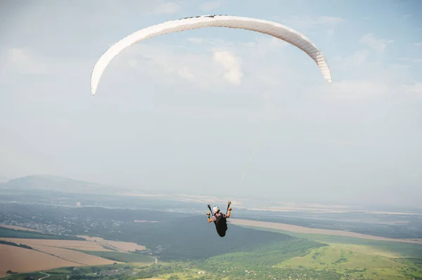 Professional paraglider in a cocoon suit flies high above the ground against the sky and fields — Stock Photo, Image