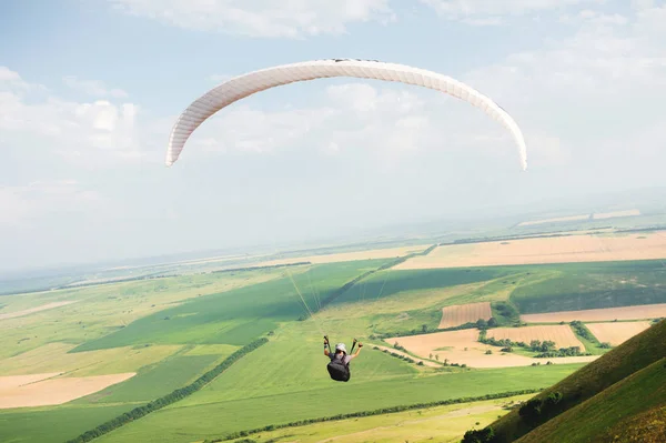 Parapente profesional en un traje de capullo vuela por encima del suelo contra el cielo y los campos — Foto de Stock