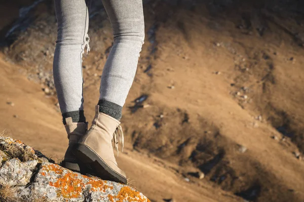 Primer plano de las piernas femeninas en botas de montaña con estilo de pie en la cima de un acantilado en el fondo de una pendiente de montaña — Foto de Stock