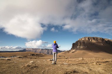 Portre bir ceket bir kap ve bir sırt çantası ile bir kız gezgin arkasından kayalar ile destansı bir manzara arka plan üzerinde duruyor