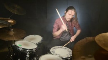 Uzun saçlı bir davulcu karanlık bir odada bir davul kiti siyah bir arka planda çalmaya başlar. Rock müzisyeni. Statik plan. Geniş açı