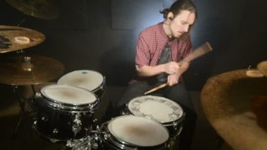 Uzun saçlı davulcular davul kiti karanlık bir odada bir siyah arka plan üzerinde oynamak. Rock müzisyeni. Statik plan. Geniş açı