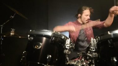 Uzun saçlı davulcular davul kiti karanlık bir odada bir siyah arka plan üzerinde oynamak. Rock müzisyeni. Statik plan. Geniş açı