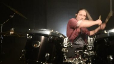 Uzun saçlı davulcular davul kiti karanlık bir odada bir siyah arka plan üzerinde oynamak. Rock müzisyeni. Statik plan. Geniş açı