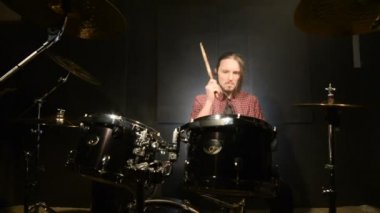 Uzun saçlı davulcular davul kiti karanlık bir odada bir siyah arka plan üzerinde oynamak. Rock müzisyeni. Statik plan. Geniş açı