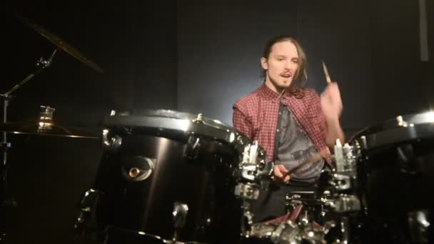 El baterista de pelo largo termina de tocar el tambor en una habitación oscura sobre un fondo negro. Músico de rock. Plan estático. Ángulo ancho — Vídeo de stock