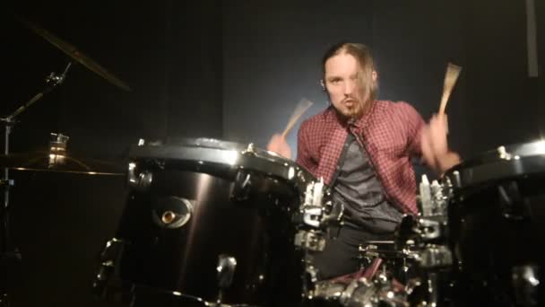 Los bateristas de pelo largo tocan el kit de batería en una habitación oscura sobre un fondo negro. Músico de rock. Plan estático. Ángulo ancho — Vídeos de Stock