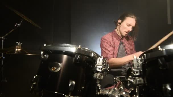 Los bateristas de pelo largo tocan el kit de batería en una habitación oscura sobre un fondo negro. Músico de rock. Plan estático. Ángulo ancho — Vídeo de stock