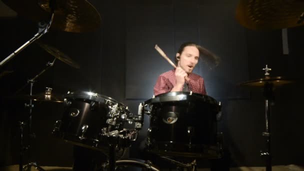 O baterista de cabelos compridos termina de tocar o tambor em uma sala escura em um fundo preto. Músico de rock. Plano estático. Ângulo largo — Vídeo de Stock