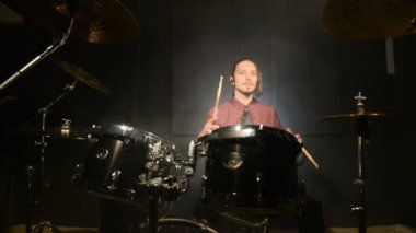 Beat şarkı intro üzerinde müzik davul sopa el ile ayarla davul oturan uzun saçlı bir davulcu sways. davul çalma zevk. Statik plan. Geniş açı