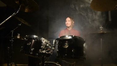 Uzun saçlı bir davulcu bir davul kiti oturan bir vape ile asılı. Vape kültür müzik. Statik plan