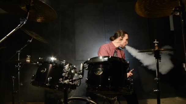 Een langharige drummer zitten achter een drumstel is met een vape zweven. Vape cultuur in muziek. Statische plan — Stockvideo