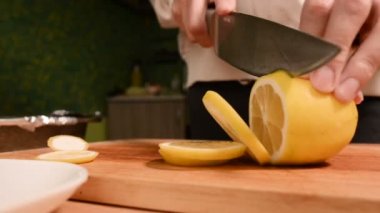 Closeup ev mutfak ahşap kesme tahtası üzerinde bir kıza el. Sarı limon gezginci üzerinde keser. Ev yemekleri