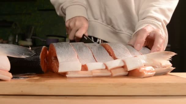 Gros plan des mains des femmes coupent avec un couteau un gros saumon sur une table en bois de cuisine maison — Video