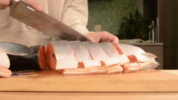 女性双手的特写镜头正在家庭烹饪的木桌上用刀切割一条大三文鱼 — 图库视频影像