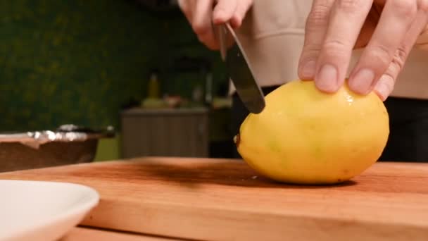 Primer plano de las manos de una niña en la cocina del hogar en una tabla de cortar de madera. Corta un limón amarillo en el cochecito. Cocina casera — Vídeo de stock